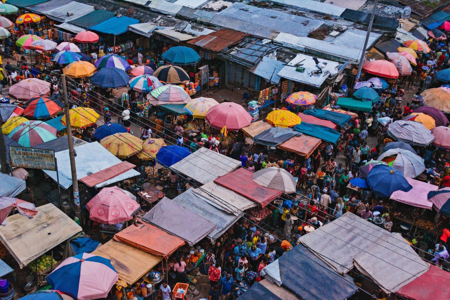 A crowded open-air market in Aba, Nigeria, seen from above, with rows of stalls under colourful umbrellas.